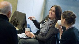 A seated woman talks animatedly to colleagues.