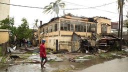A man walking through a flooded street in front of a destroyed building.