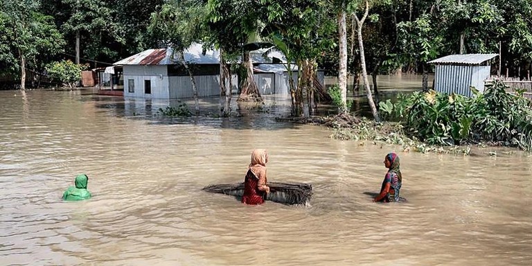Three women try to walk while almost completely submerged in flood water. 