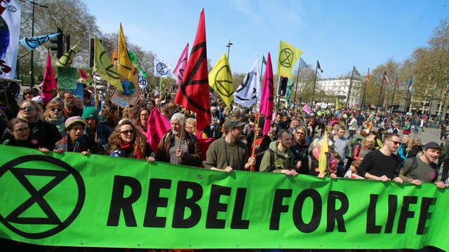 Extinction Rebellion climate protesters march through London behind a big green banner proclaiming 'Rebel for life'