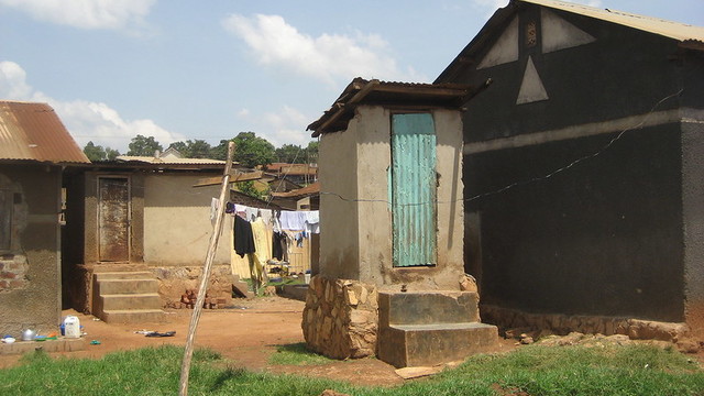 A small brick building with two steps leading to a corrugated iron door houses a pit latrine.