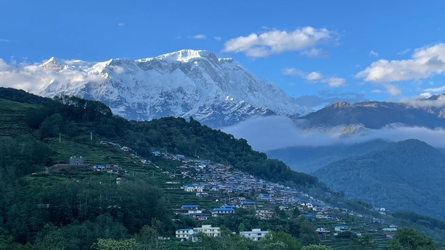 View of a mountain with a few houses. Snowed mountains in the background. 